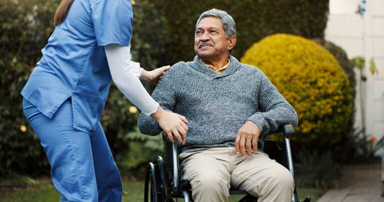 Adult child and senior parent sitting together and smiling in a bright, home-like assisted living apartment.
