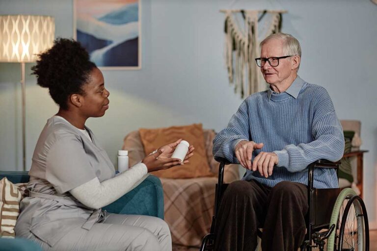An adult daughter gently holding her elderly mother's hand at a table with paperwork and a cup of tea nearby.