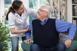 Older adult arranging family photos and clothing in a bright assisted living room with a family member nearby.