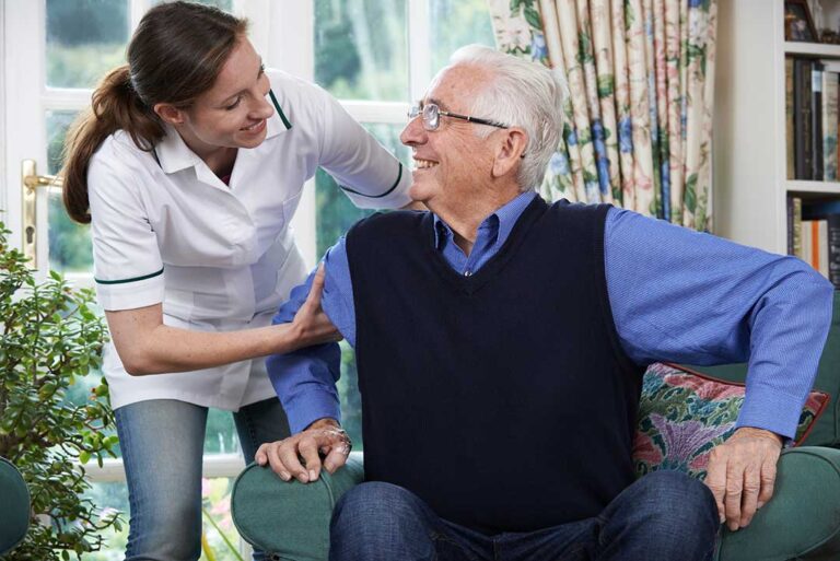 Older adult arranging family photos and clothing in a bright assisted living room with a family member nearby.